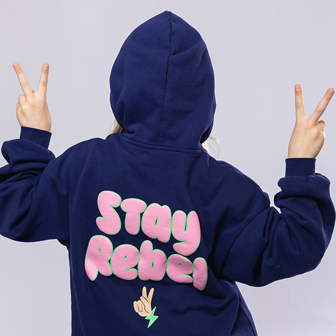 Girl wearing a navy blue hoodie with "Stay Rebel" text in pink and green, with a cute peace sign