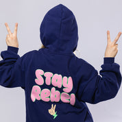 Girl wearing a navy blue hoodie with "Stay Rebel" text in pink and green, with a cute peace sign
